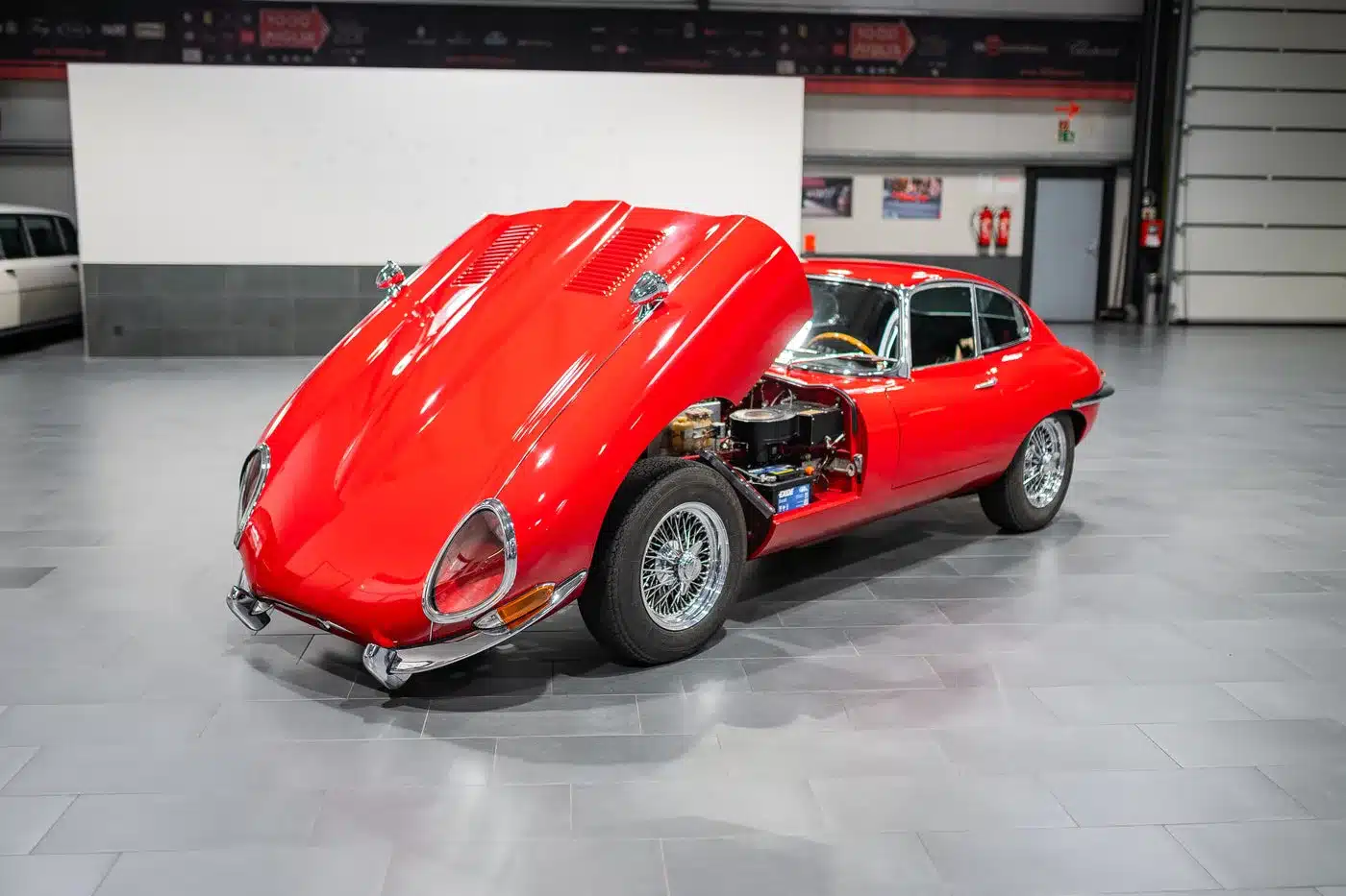 Roter Jaguar E-Type Serie 1 4.2 Roadster von 1965 mit geöffneter Motorhaube, ausgestellt in einer modernen Halle.