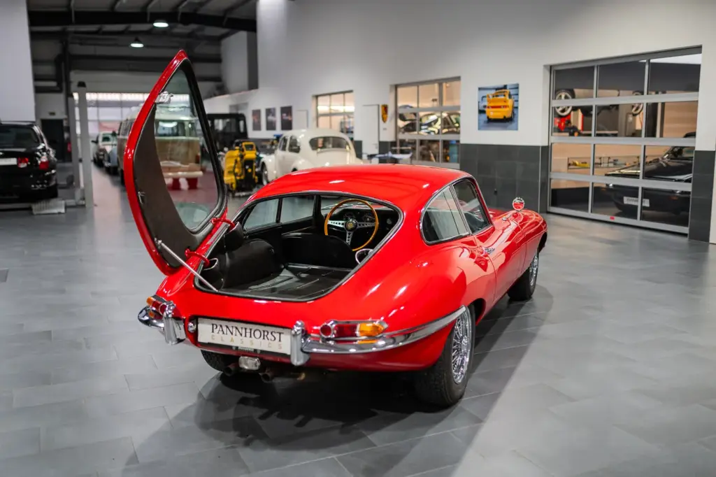 Roter Jaguar E-Type Coupé mit geöffneter Heckklappe in einer Werkstattumgebung, Blick von hinten rechts.