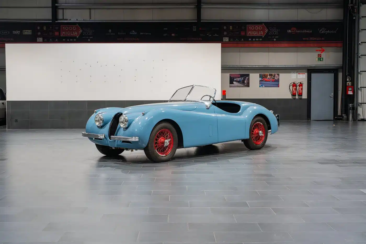 Blaue Jaguar Karosserie, seitlich fotografiert, mit roten Felgen in einer Ausstellungshalle.