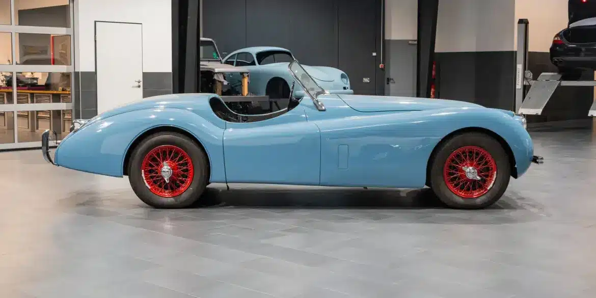 Seitenansicht einer blauen Jaguar Karosserie mit roten Speichenrädern in einer modernen Werkstatt