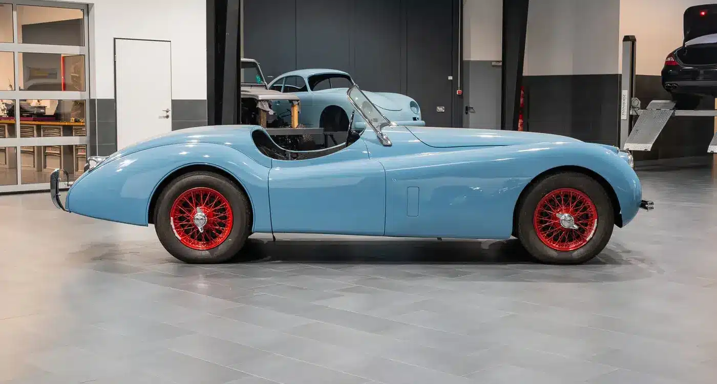 Seitenansicht einer blauen Jaguar Karosserie mit roten Speichenrädern in einer modernen Werkstatt