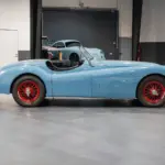 Seitenansicht einer blauen Jaguar Karosserie mit roten Speichenrädern in einer modernen Werkstatt