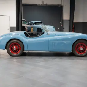 Seitenansicht einer blauen Jaguar Karosserie mit roten Speichenrädern in einer modernen Werkstatt