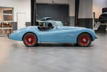Seitenansicht einer blauen Jaguar Karosserie mit roten Speichenrädern in einer modernen Werkstatt
