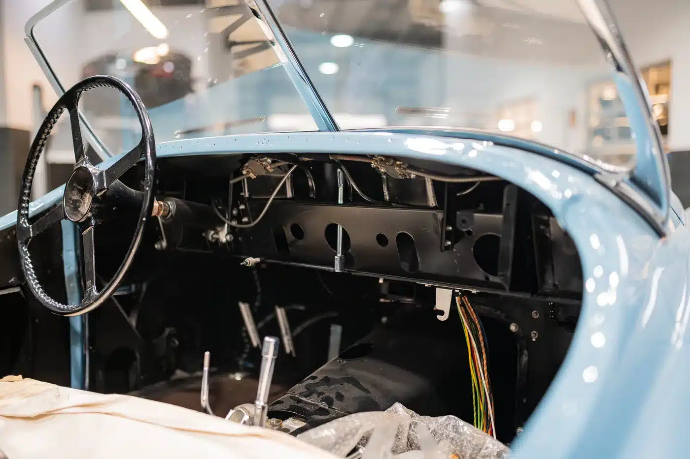 Detailaufnahme des Innenraums einer blauen Jaguar Karosserie ohne Innenausstattung, sichtbar ist das Lenkrad und die Elektrik während der Restauration.