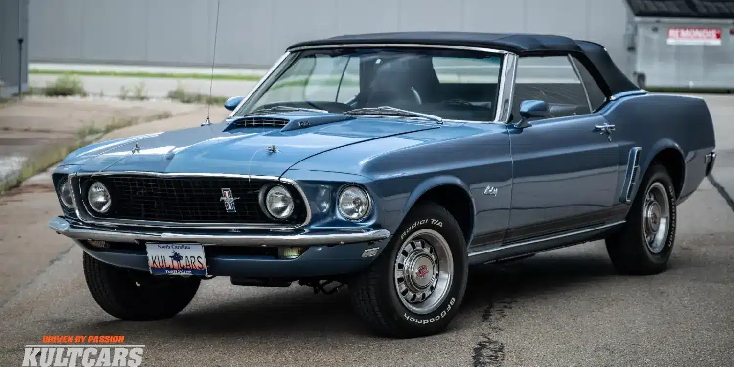 Ford Mustang 428 Cobra Jet Convertible von 1969 in blau, Cabrio mit geschlossenem Verdeck, Front- und Seitenansicht, auf einem Parkplatz.