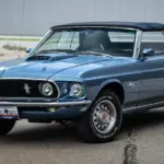 Ford Mustang 428 Cobra Jet Convertible von 1969 in blau, Cabrio mit geschlossenem Verdeck, Front- und Seitenansicht, auf einem Parkplatz.