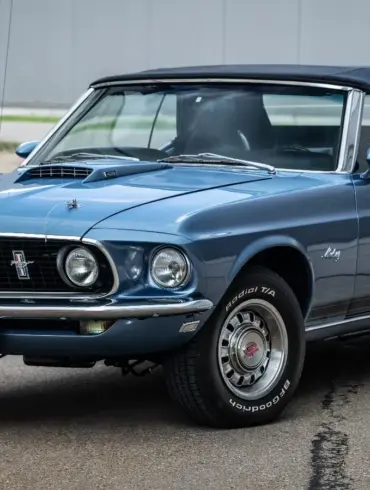 Ford Mustang 428 Cobra Jet Convertible von 1969 in blau, Cabrio mit geschlossenem Verdeck, Front- und Seitenansicht, auf einem Parkplatz.