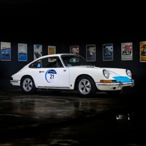 Seitenansicht eines weißen klassischen Sportwagens mit Startnummer, ausgestellt vor Motorsport-Postern.