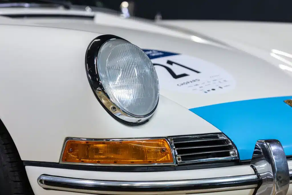 Nahaufnahme eines weißen Sportwagens mit Chromelementen und Startnummer auf dem Kotflügel