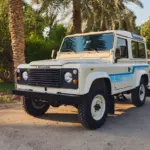 Weißer Land Rover 90 aus dem Jahr 1985 im Freien vor Palmen und Grünanlage.