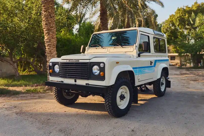 Weißer Land Rover 90 aus dem Jahr 1985 im Freien vor Palmen und Grünanlage.