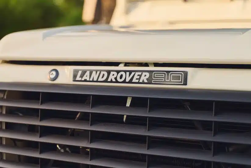 Nahaufnahme vom Kühlergrill mit Land Rover 90 Emblem eines klassischen Geländewagens, Baujahr 1985, in Elfenbeinweiß.