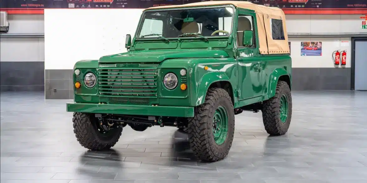 Land Rover Defender 90 TD5 Cabriolet in Belize Green mit cremefarbener Plane, frontal in einer Halle aufgenommen