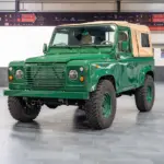 Land Rover Defender 90 TD5 Cabriolet in Belize Green mit cremefarbener Plane, frontal in einer Halle aufgenommen