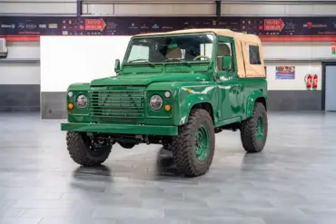 Land Rover Defender 90 TD5 Cabriolet in Belize Green mit cremefarbener Plane, frontal in einer Halle aufgenommen