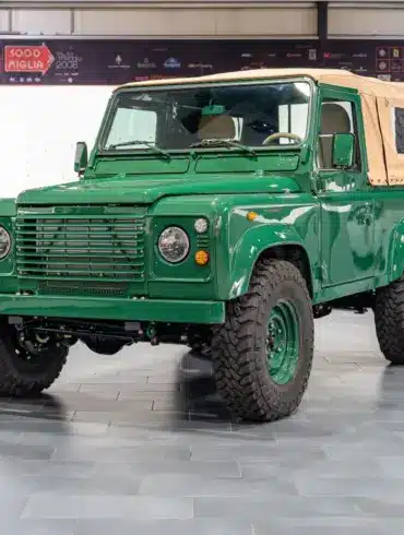 Land Rover Defender 90 TD5 Cabriolet in Belize Green mit cremefarbener Plane, frontal in einer Halle aufgenommen