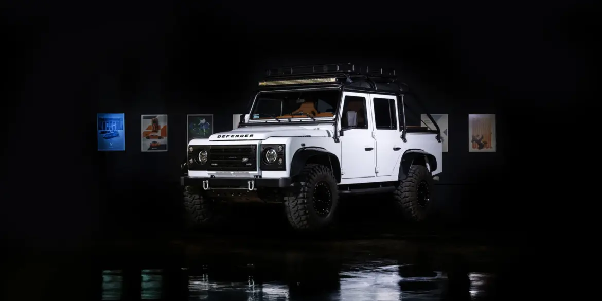 Weißer Land Rover Defender mit Offroad-Reifen im Studio, reflektiert auf glänzendem Boden.