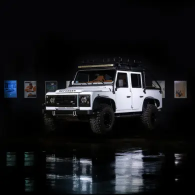 Weißer Land Rover Defender mit Offroad-Reifen im Studio, reflektiert auf glänzendem Boden.