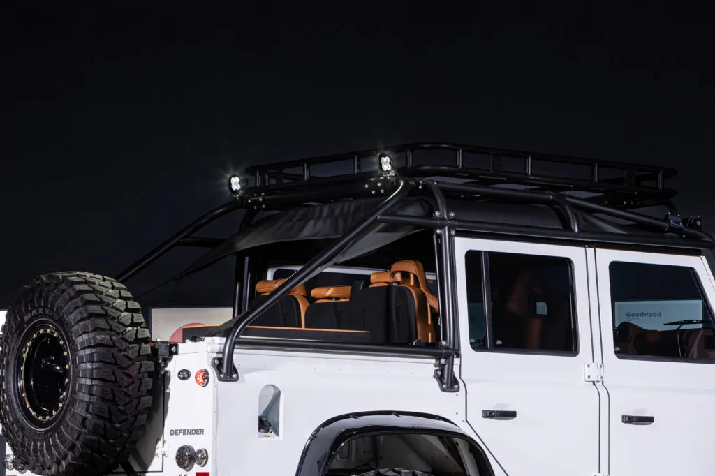 Heck und Dach eines weißen Land Rover Defender mit Reserverad und Dachgepäckträger vor dunklem Hintergrund