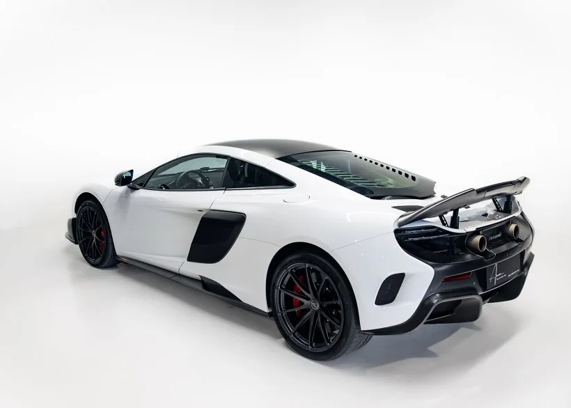 Heckansicht eines weißen McLaren 675LT mit großem Carbon-Heckflügel und schwarzen Felgen in einem Studio.