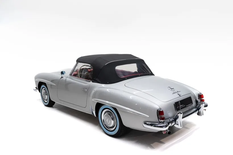 Silberner Mercedes-Benz 190 SL Cabriolet von 1957 mit geschlossenem schwarzen Stoffverdeck, fotografiert von hinten schräg seitlich auf weißem Hintergrund.