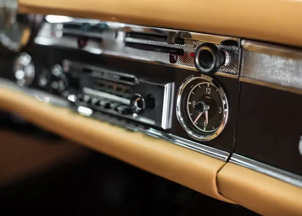 Detailansicht des Armaturenbretts mit Uhr und Radio in einer restaurierten Mercedes-Benz 230 SL Pagode, beige Lederausstattung.