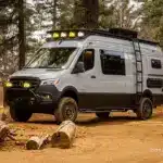 Mercedes-Benz Sprinter 170 High Roof Offroad-Ausbau 'Güero' mit Dachträger, Zusatzscheinwerfern und Expeditionsausstattung im Wald.