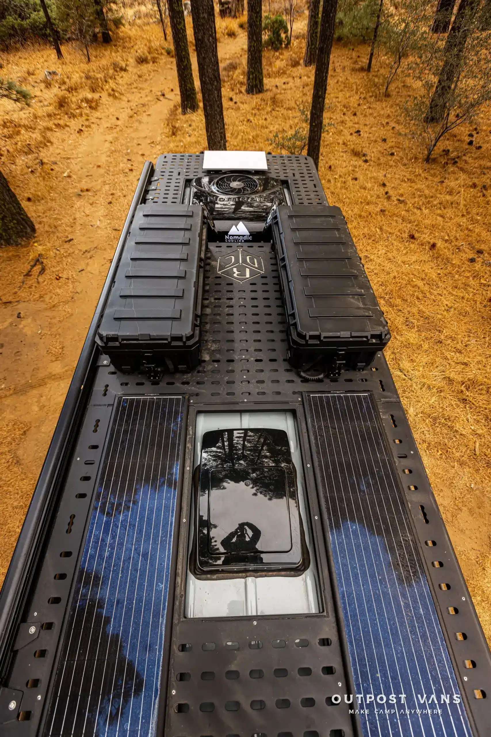 Dach eines Mercedes Sprinter Güero mit Solarmodulen, schwarzen Expeditionsboxen und Dachträger im Wald.