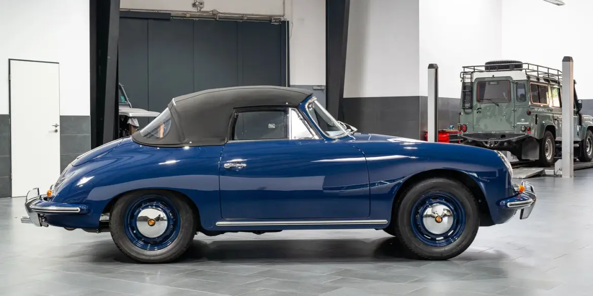 Blaues Porsche 356 C Cabriolet von 1964 mit geschlossenem schwarzen Stoffverdeck in einer Halle, Seitenansicht.
