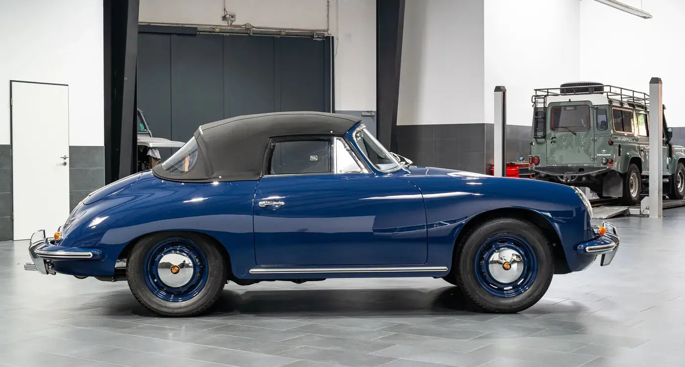 Blaues Porsche 356 C Cabriolet von 1964 mit geschlossenem schwarzen Stoffverdeck in einer Halle, Seitenansicht.