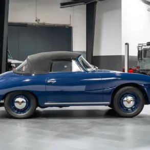 Blaues Porsche 356 C Cabriolet von 1964 mit geschlossenem schwarzen Stoffverdeck in einer Halle, Seitenansicht.