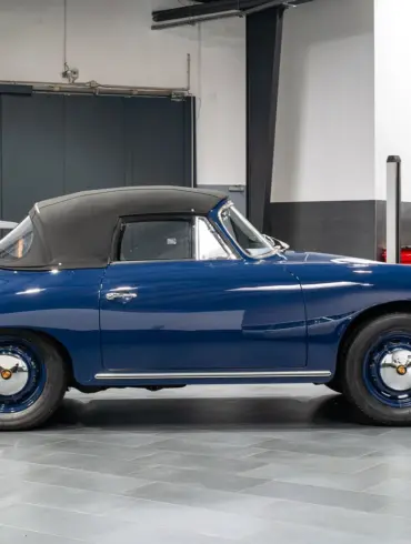 Blaues Porsche 356 C Cabriolet von 1964 mit geschlossenem schwarzen Stoffverdeck in einer Halle, Seitenansicht.