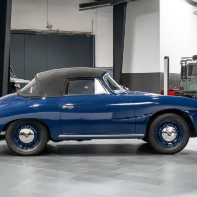 Blaues Porsche 356 C Cabriolet von 1964 mit geschlossenem schwarzen Stoffverdeck in einer Halle, Seitenansicht.