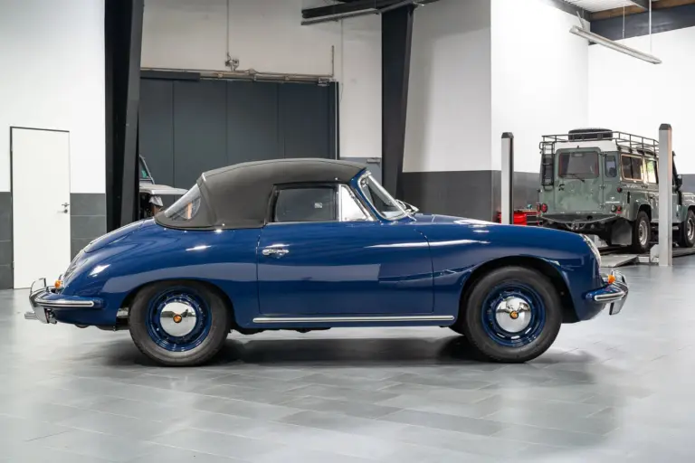 Blaues Porsche 356 C Cabriolet von 1964 mit geschlossenem schwarzen Stoffverdeck in einer Halle, Seitenansicht.