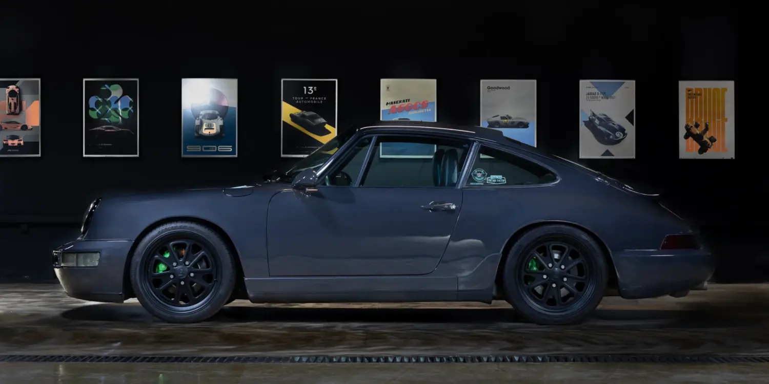 Dunkelgrauer Porsche 911 (964) Carrera 2, Baujahr 1991, mit schwarzen Felgen und grünen Akzenten, seitlich fotografiert in einer Ausstellungshalle