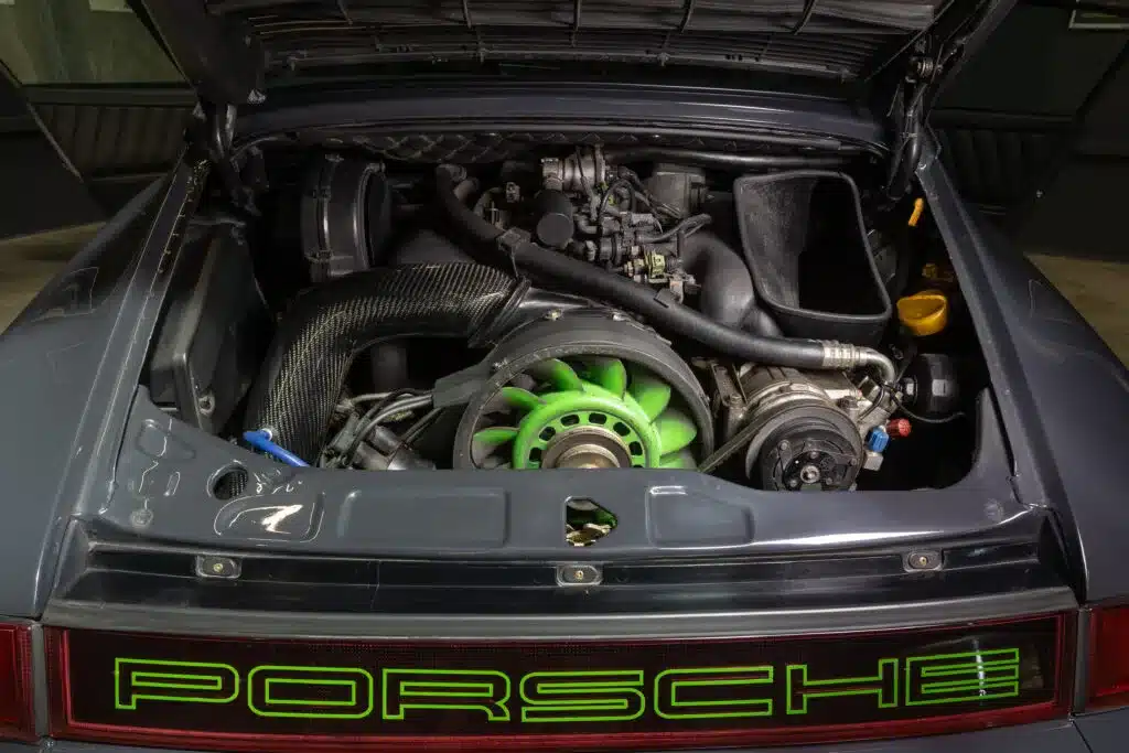 Der geöffnete Motorraum eines Porsche 911 (964) Carrera 2 mit sichtbarem 3,6-Liter-Boxermotor und grünem Lüfterrad.