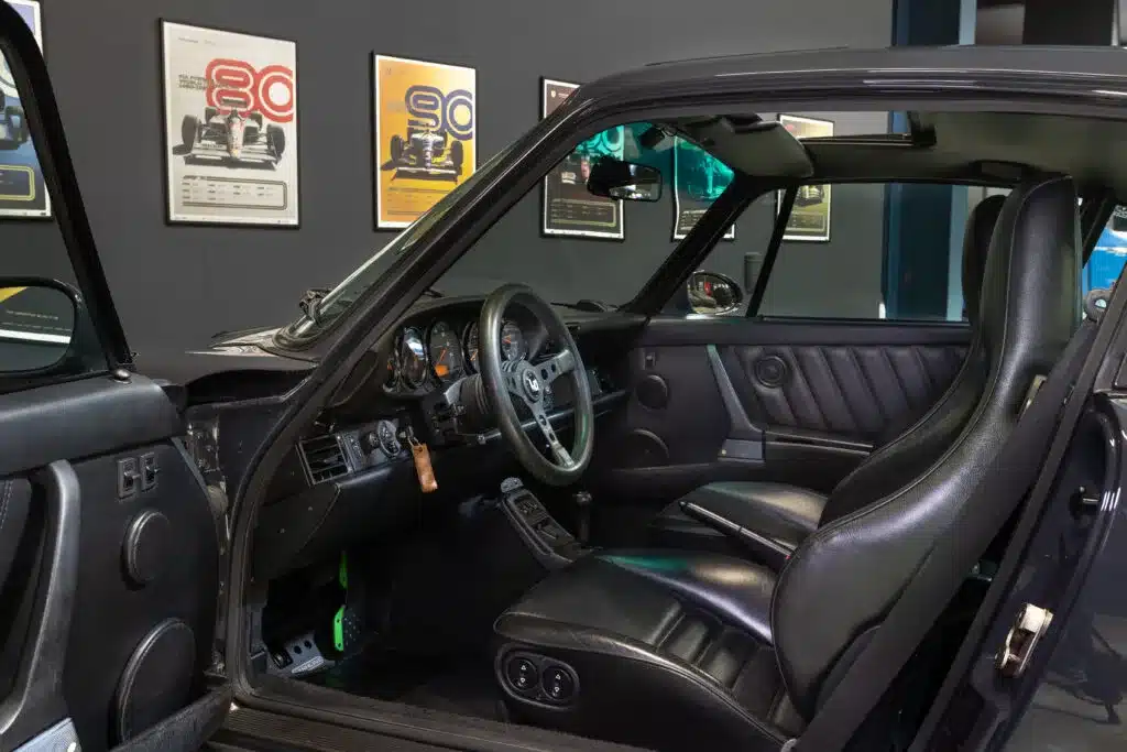 Innenraum eines Porsche 911 (964) Carrera 2 mit schwarzem Leder und klassischem Armaturenbrett, Blick durch die geöffnete Tür.