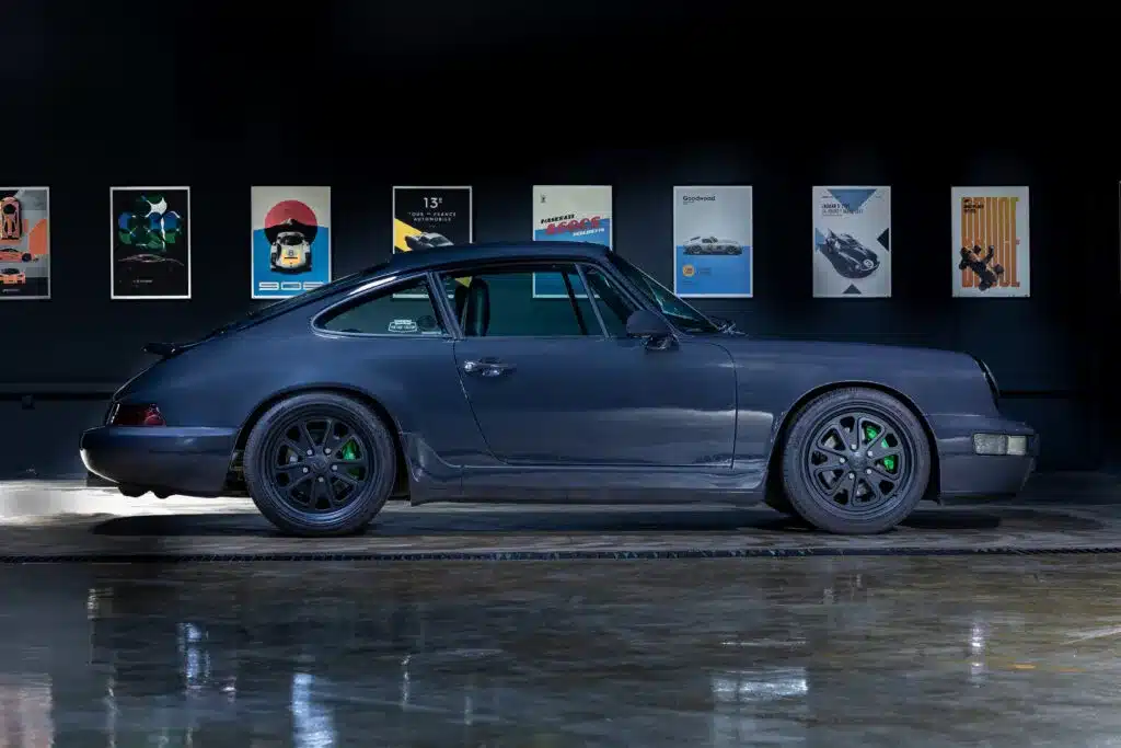 Dunkelgrauer Porsche 911 (964) Carrera 2 mit schwarzen Walker-Rädern und grünen Akzenten in seitlicher Ansicht vor dunklem Hintergrund.
