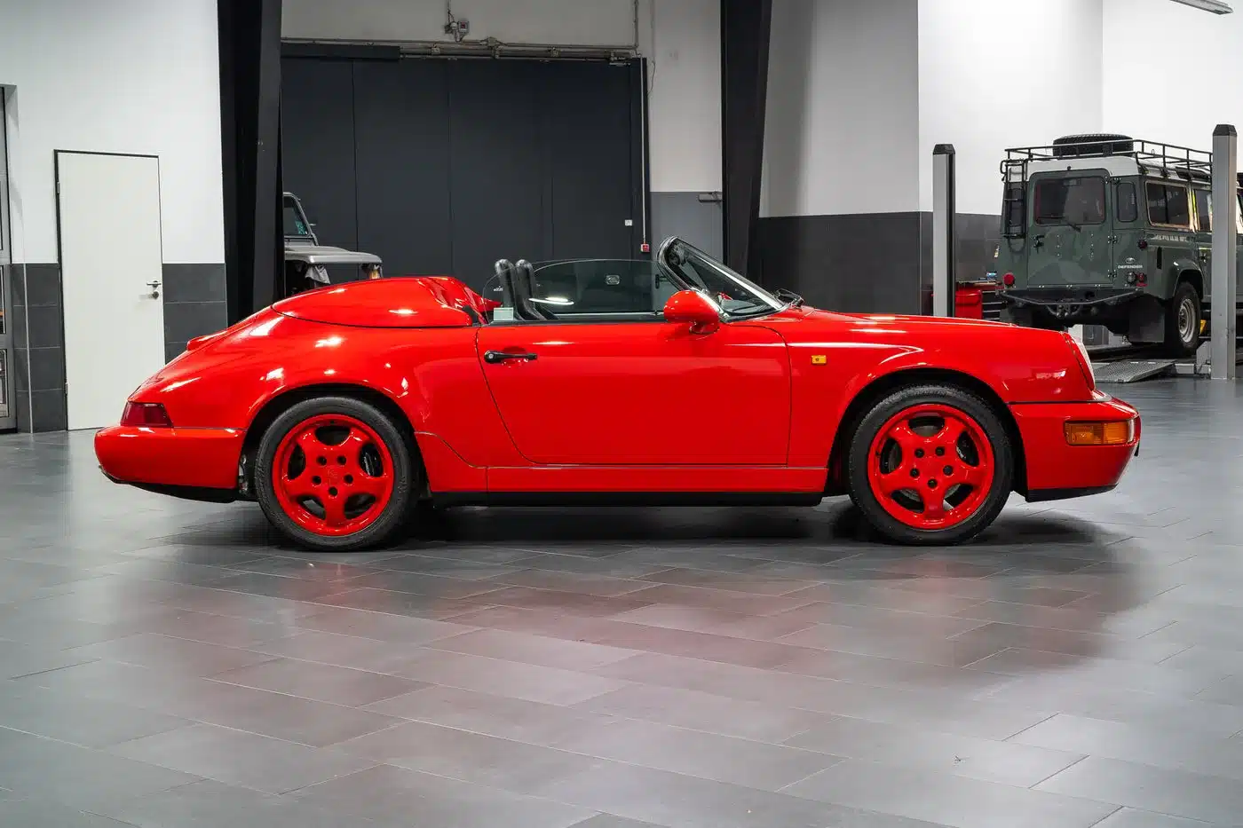 Seitliche Ansicht eines Porsche 911 (964) Carrera Speedster in Indischrot, Cabrio-Dach offen, in einer Werkstatthalle.