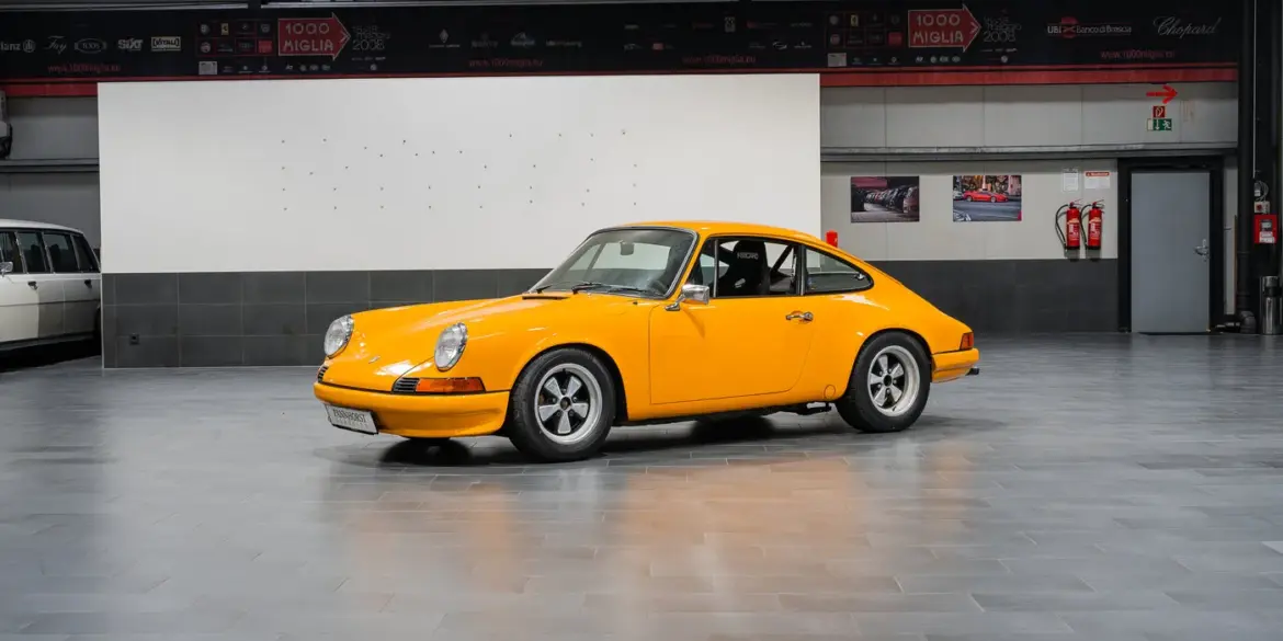 Gelber Porsche 911 der ersten Generation, seitlich fotografiert, in einer modernen Halle.