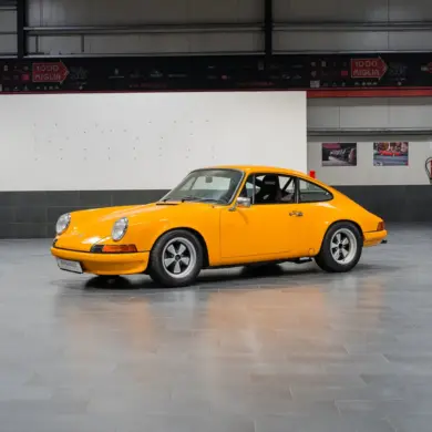 Gelber Porsche 911 der ersten Generation, seitlich fotografiert, in einer modernen Halle.