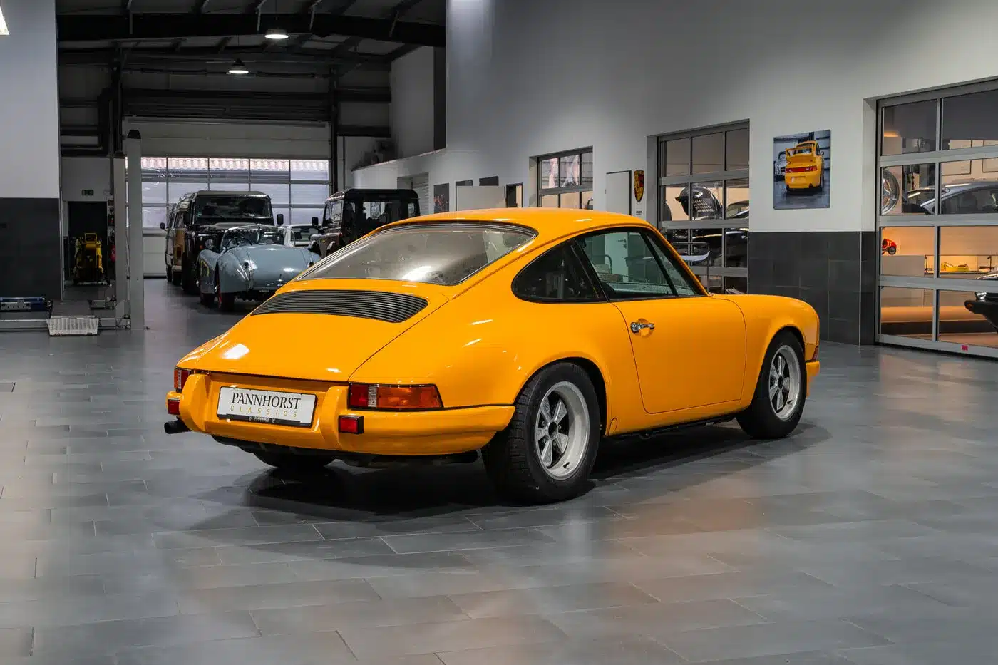 Gelber Porsche 911 der frühen Generation in einer modernen Fahrzeughalle, Heckansicht.