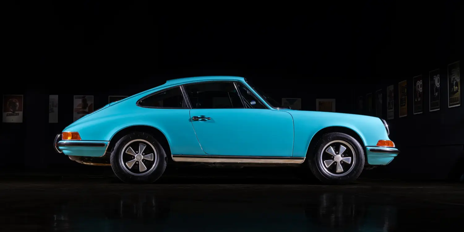Türkiser Porsche 911T aus dem Jahr 1971, seitliche Ansicht in dunkler Umgebung, Fuchs-Leichtmetallräder sichtbar.