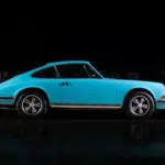Türkiser Porsche 911T aus dem Jahr 1971, seitliche Ansicht in dunkler Umgebung, Fuchs-Leichtmetallräder sichtbar.