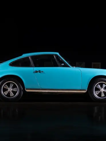 Türkiser Porsche 911T aus dem Jahr 1971, seitliche Ansicht in dunkler Umgebung, Fuchs-Leichtmetallräder sichtbar.