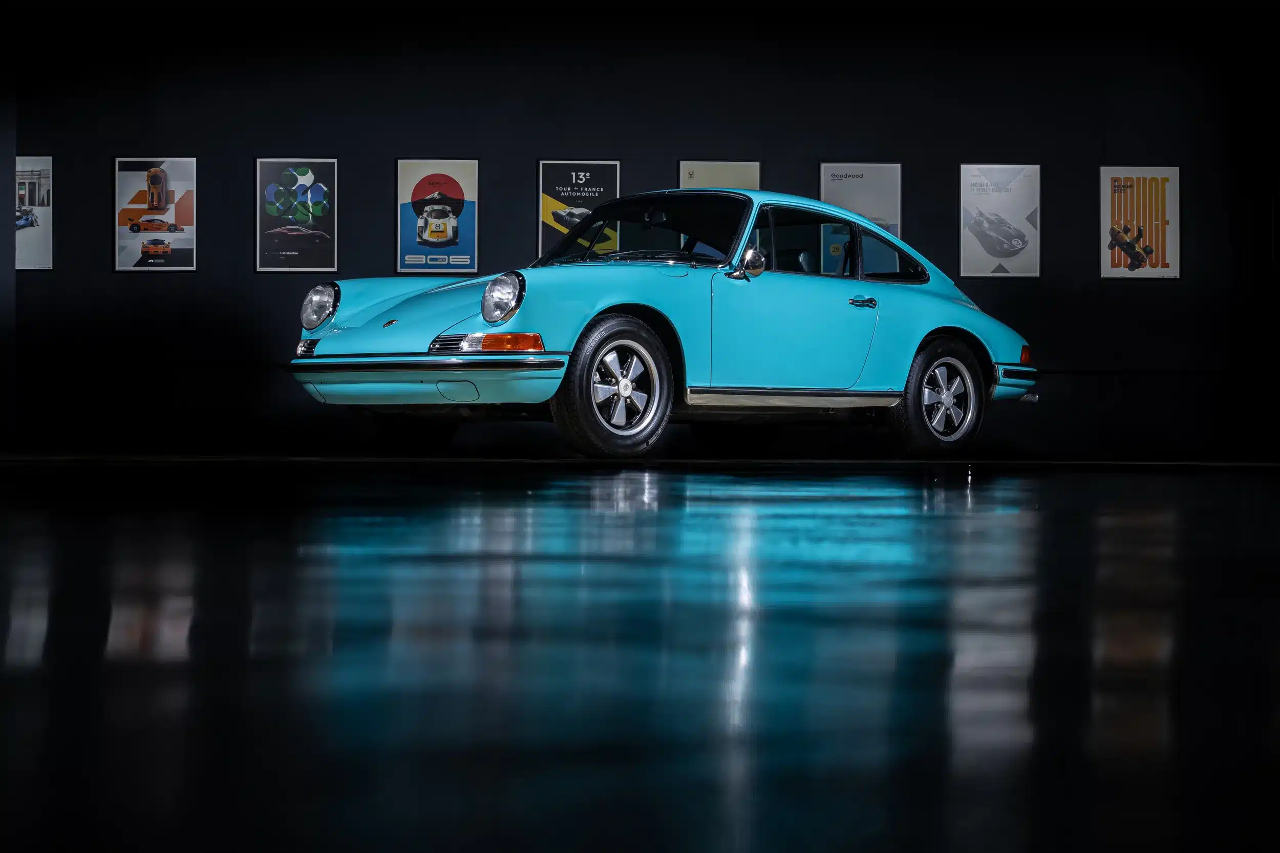 Türkiser Porsche 911T aus dem Jahr 1971 im Ausstellungsraum, seitliche Ansicht vor dunklem Hintergrund mit Poster-Wand.