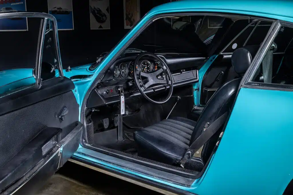Offene Fahrertür mit Blick in den Innenraum eines türkisfarbenen Porsche 911T von 1971, Leder-Innenausstattung, Armaturenbrett und Lenkrad sichtbar.
