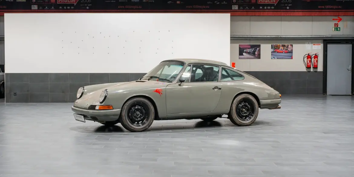 Seitenansicht eines Porsche 912 Coupé von 1966 in Zeltgrau mit schwarzen Felgen, fotografiert in einer modernen Halle.