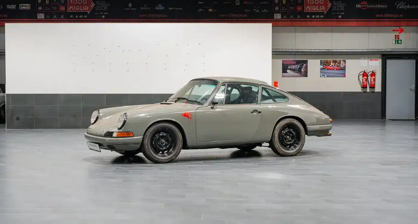 Seitenansicht eines Porsche 912 Coupé von 1966 in Zeltgrau mit schwarzen Felgen, fotografiert in einer modernen Halle.
